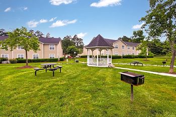 a gazebo and picnic tables in a grassy area with apartment buildings in the